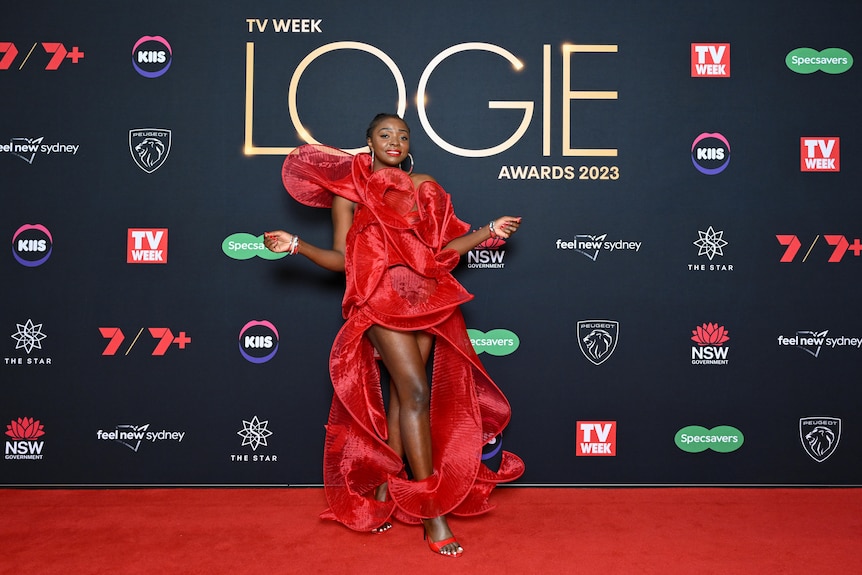 A woman wears a long red gown and poses on a red carpet