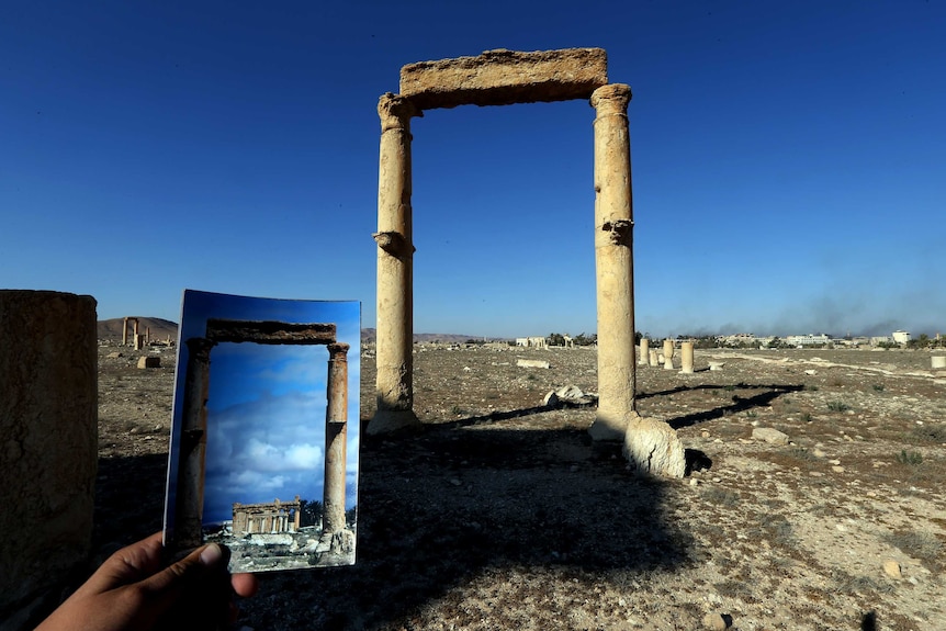 A 2014 photograph of the Temple of Baal Shamin is held in front of the damaged site.
