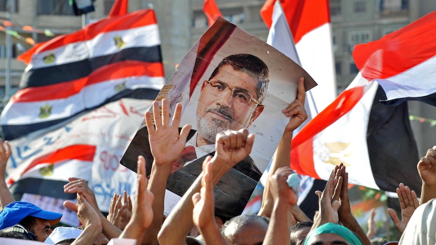 Supporters of Mohammed Morsi hold up his portrait and wave their national flag.