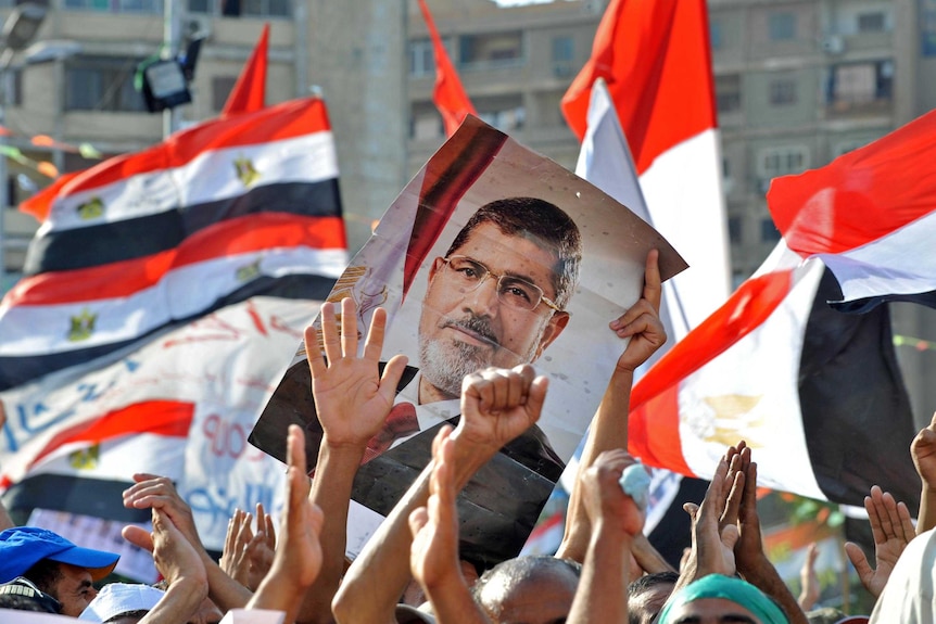 Supporters of Mohammed Morsi hold up his portrait and wave their national flag.