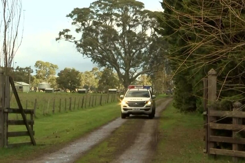 A police ute drives up a driveway with trees on the right