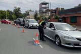 A line of cars funnel through a checkpoint manned by police.