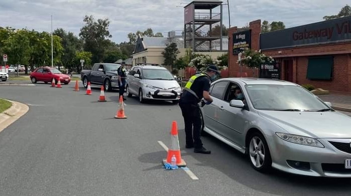 A line of cars funnel through a checkpoint manned by police.