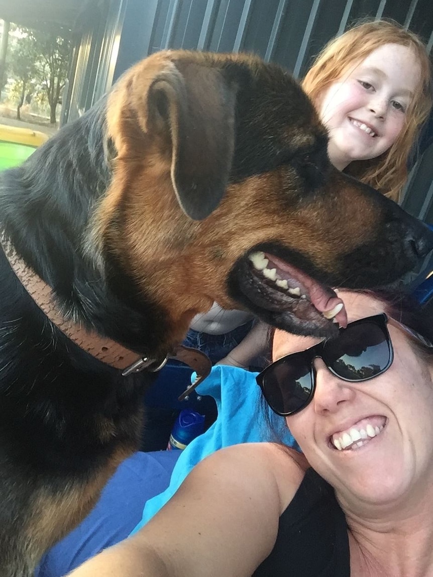 A black and tan dog, a redheaded girl and a woman in her late 30s all smile for a tight selfie.