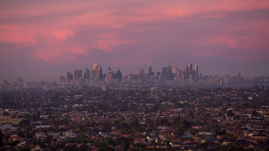 Seen from the air, the Melbourne city skyline rises above the sprawling suburbs in the pink light of dawn.