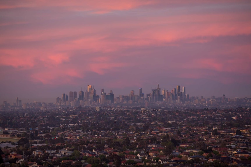Seen from the air, the Melbourne city skyline rises above the sprawling suburbs in the pink light of dawn.