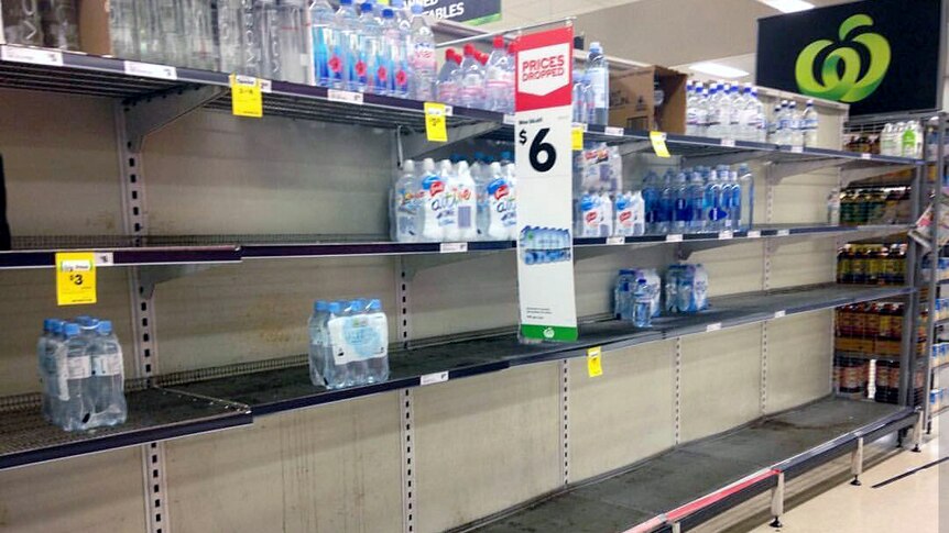 Bare shelves in a Townsville supermarket showing only a few bottles of water left.
