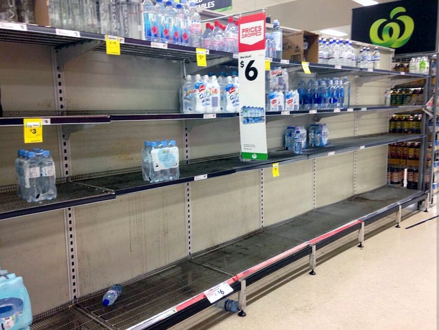 Bare shelves in a Townsville supermarket showing only a few bottles of water left.