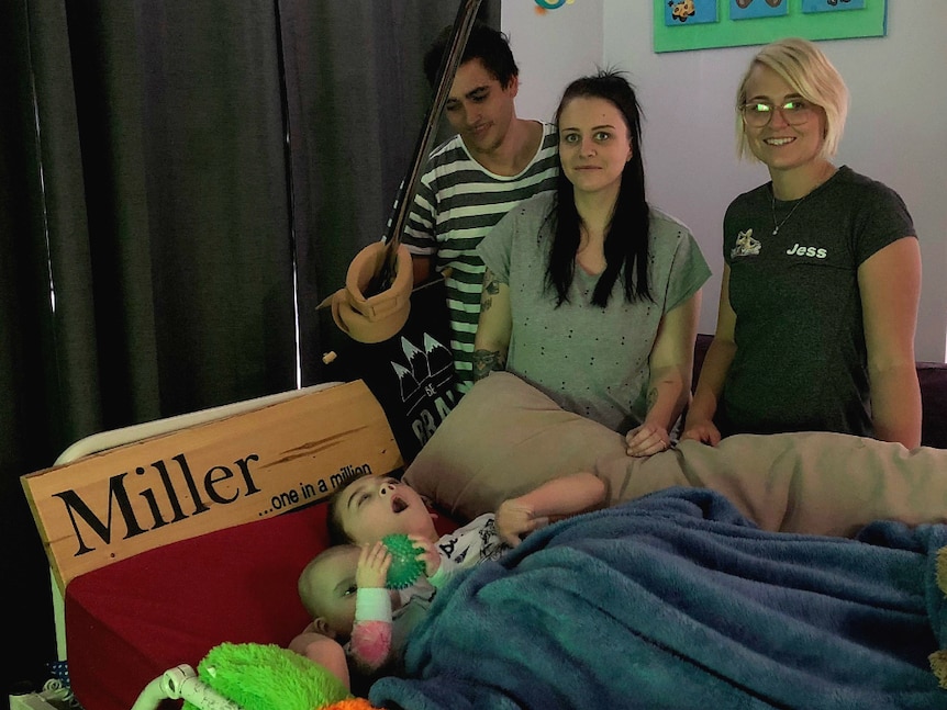 Three adults standing over an eight year old boy as he lay in a hospital bed at home.