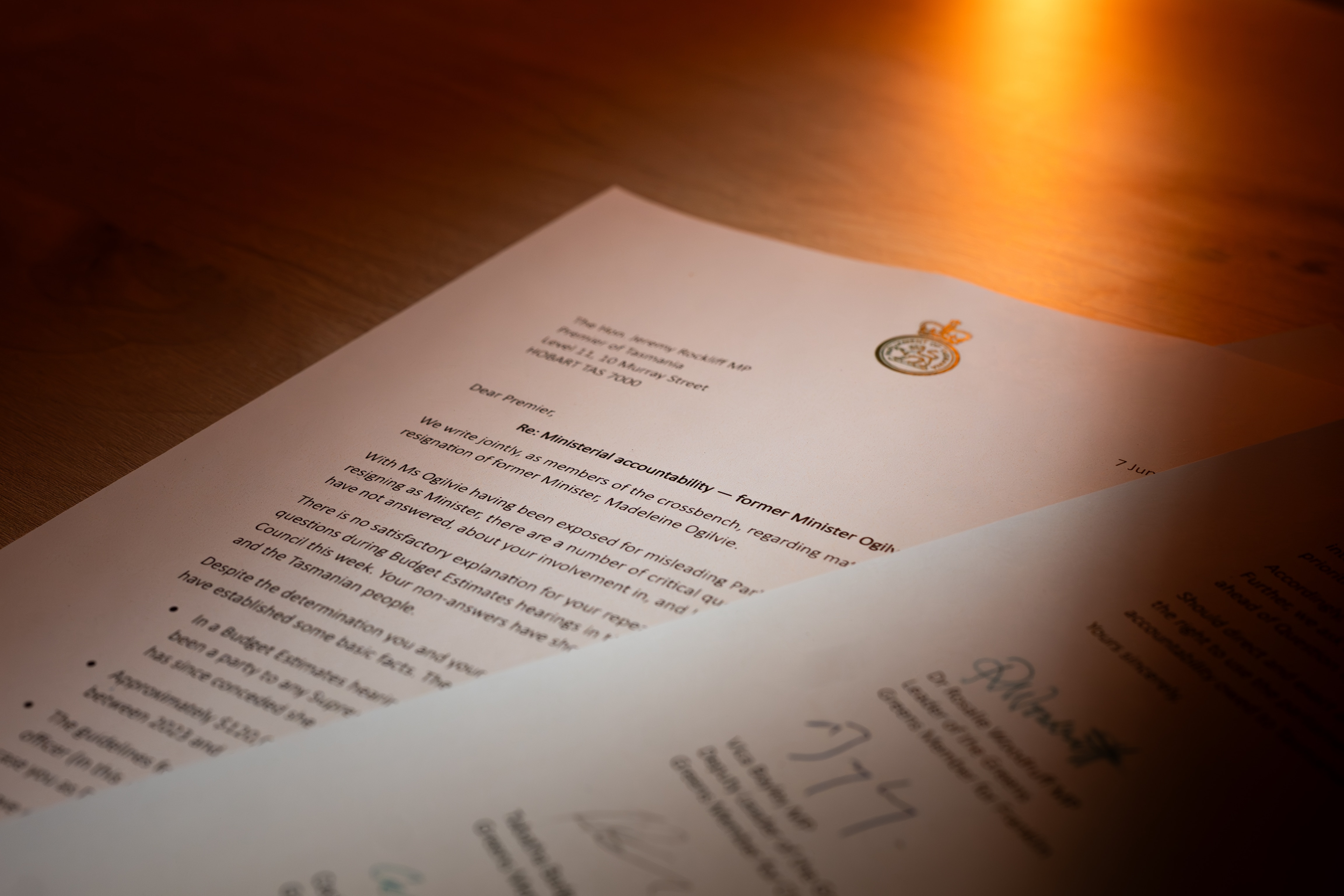 Two sheets of paper with typing on them, on a wooden desk, with a warm light behind them.