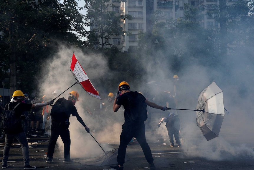 Men holding umbrellas surrounded by tear gas