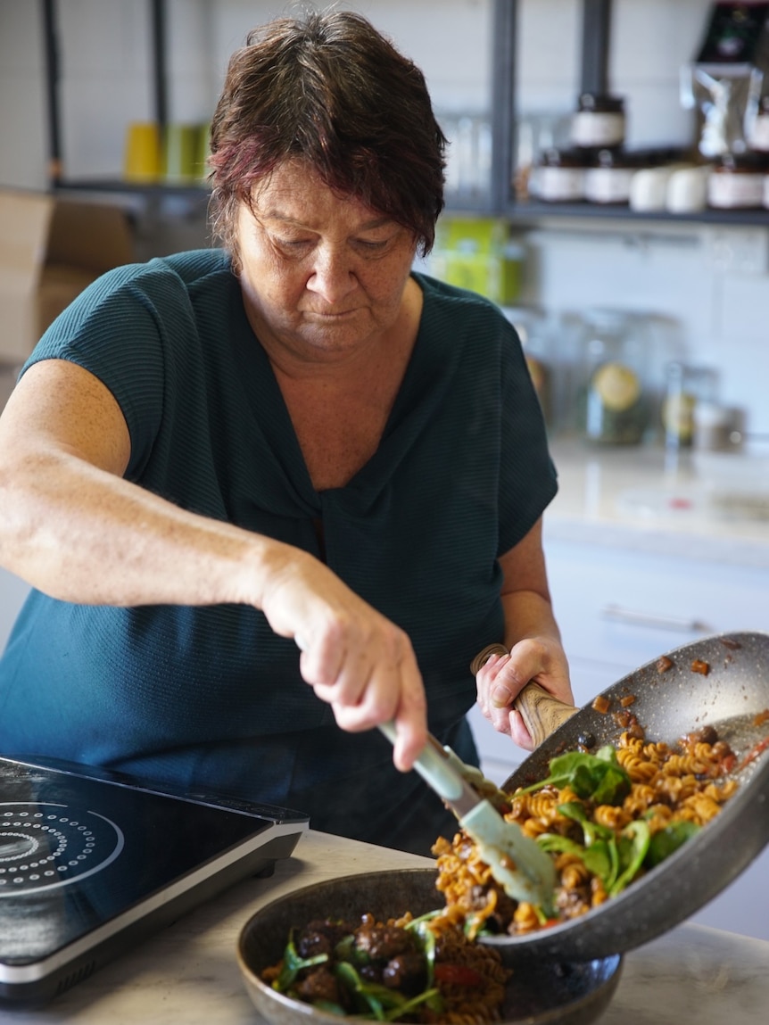 A woman with dark, short hair, transfers pasta from a pan to a bowl.