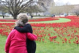 Two women hug in front of a field of poppies at the Australian War Memorial.