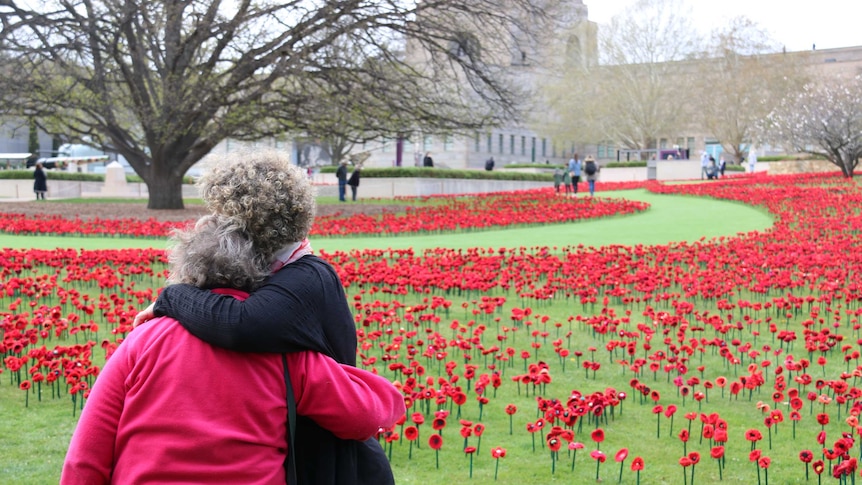 Two women hug in front of a field of poppies at the Australian War Memorial.