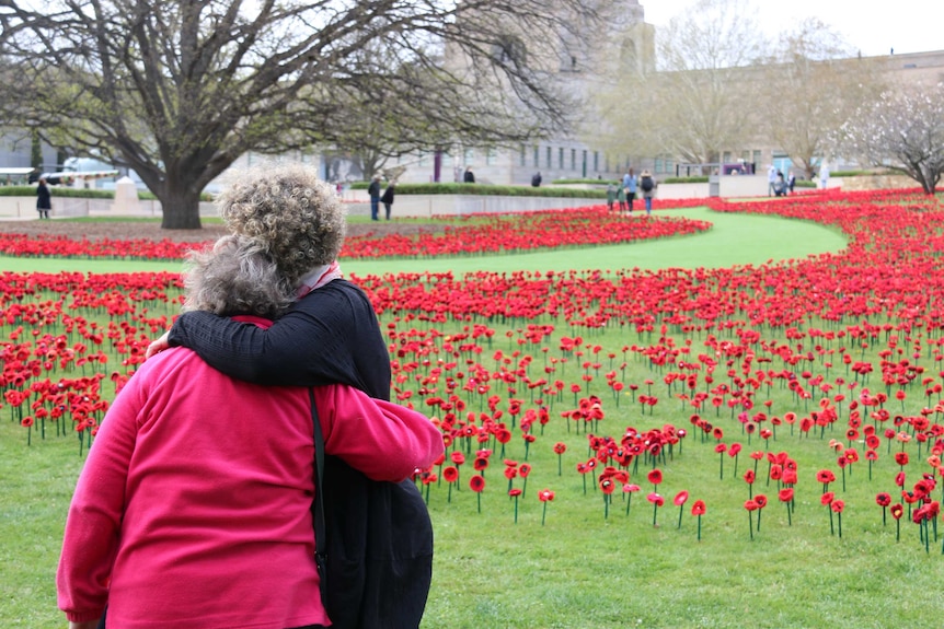 Two women hug in front of a field of poppies at the Australian War Memorial.