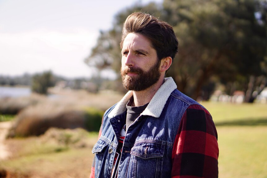 Man wearing a denim jacket looking out into the distance at a park.