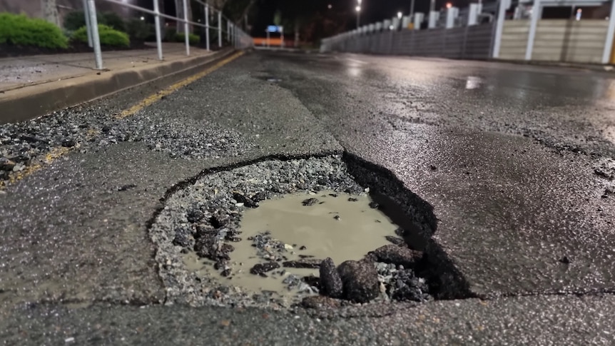 pothole half-filled with dirty water on bitumen road at night