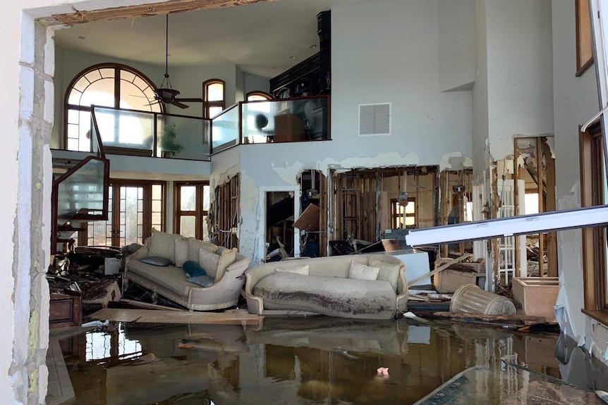 Water-damaged walls and furniture inside a large home. The floor is still wet.