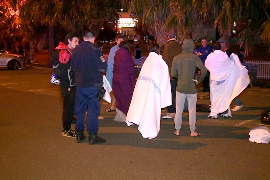 People wrapped in blankets stand on the road.