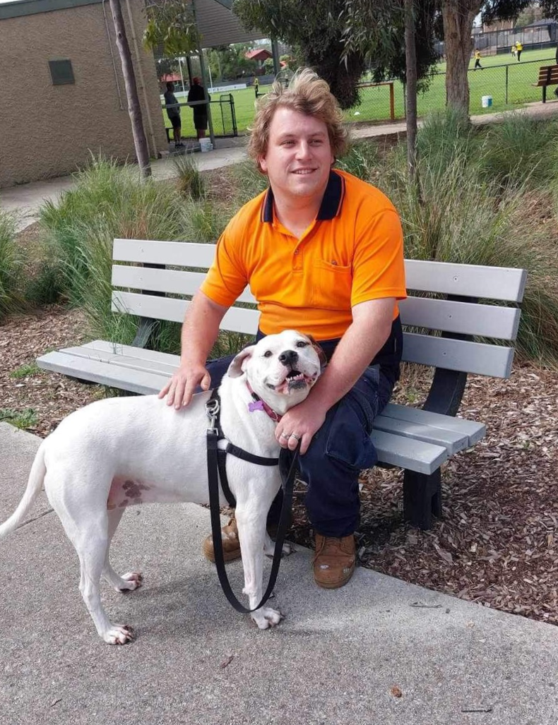 A man sits on a park bench and pats his bulldog.