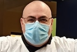 A man wears a surgical mask and surgical gown.