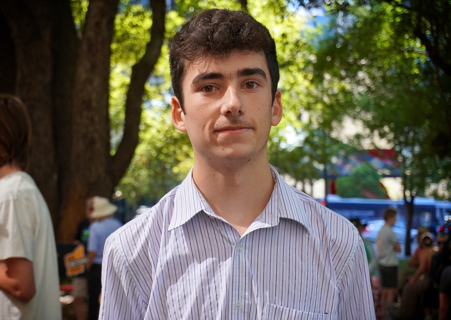 A teenage boy with a collared shirt in a park at a rally