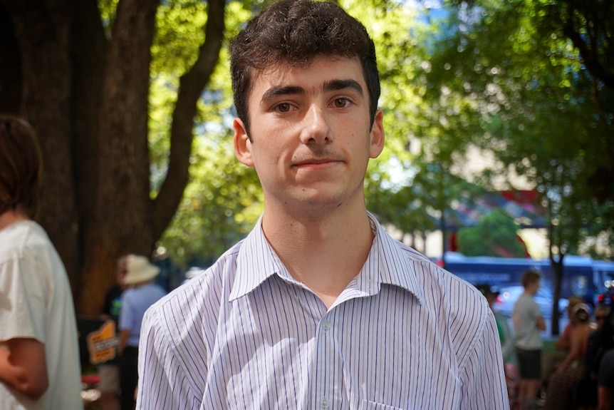 A teenage boy with a collared shirt in a park at a rally