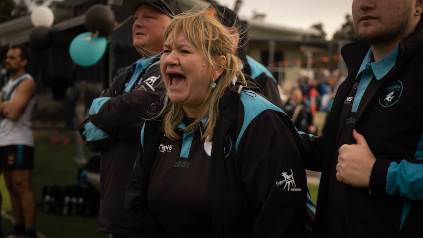A woman wearing a black and light blue jersey cheers on a football team from the sidelines
