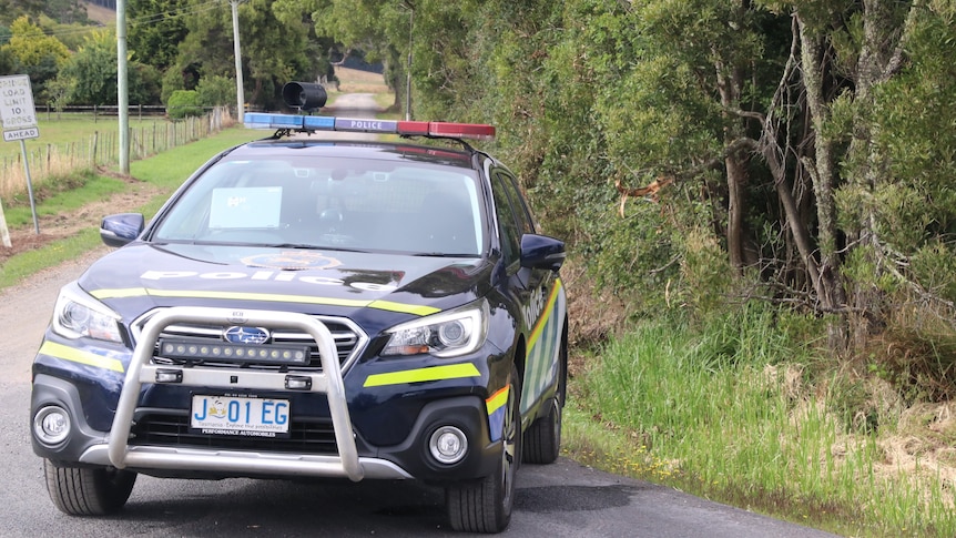 A police car parks across a country road.