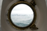 As if from the inside of a ship cabin, through a small circular window rough ocean can be seen.