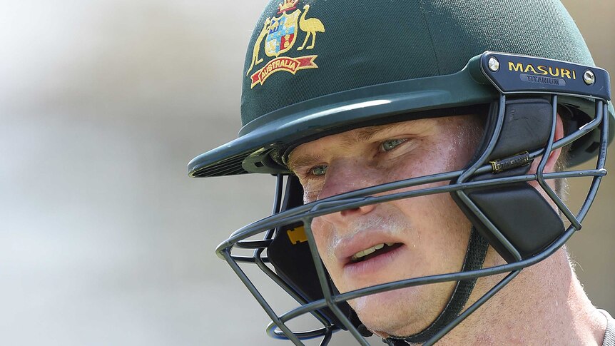 A man wearing a green cricket helmet with an Australian coat of arms looks off camera