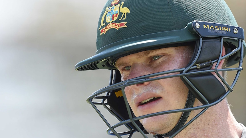 A man wearing a green cricket helmet with an Australian coat of arms looks off camera
