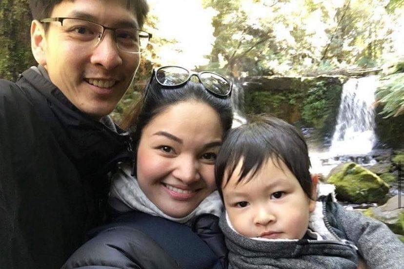 A young Thai couple cuddle their baby in front of a waterfall