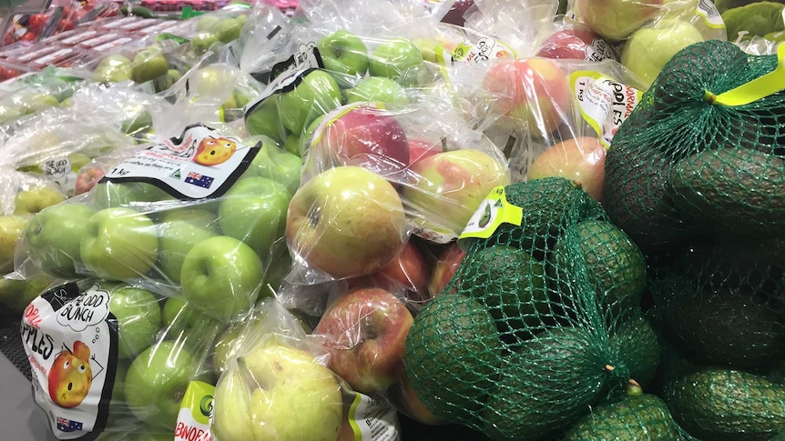 Bunches of apples and avocados wrapped in plastic and fruit netting in the supermarket
