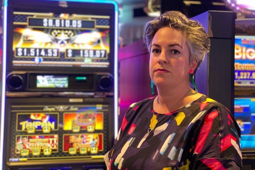 A woman with short hair standing in front of poker machines.