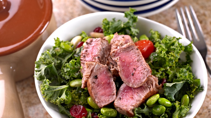 A plate of green salad with medium steak on top.