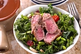 A plate of green salad with medium steak on top.