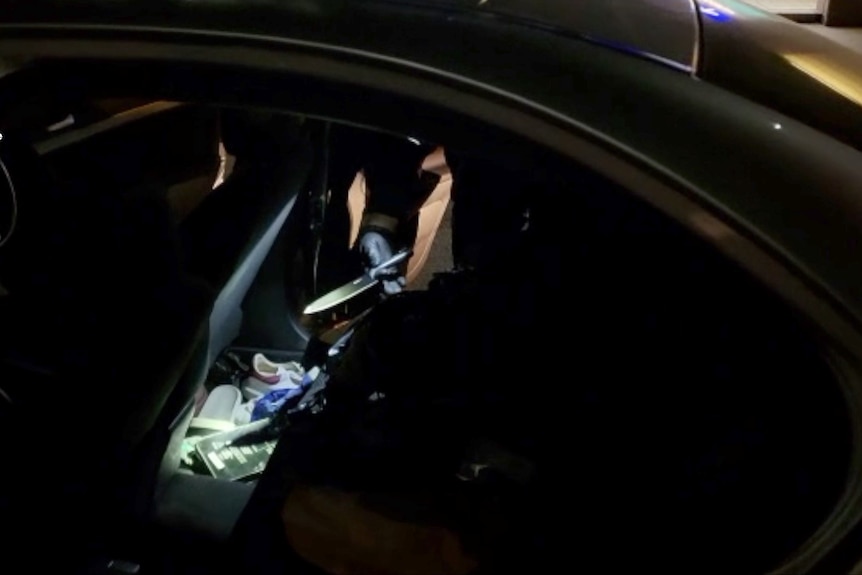A gloved hand can be seen holding up a knife found in the back seat of a car