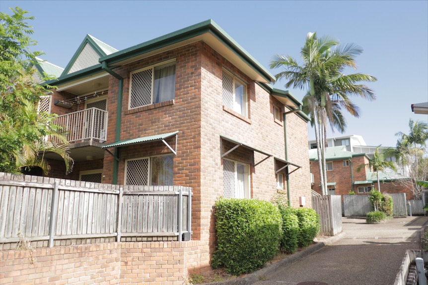A two-storey set of brick units with a green roof and wooden fencing in Annerley
