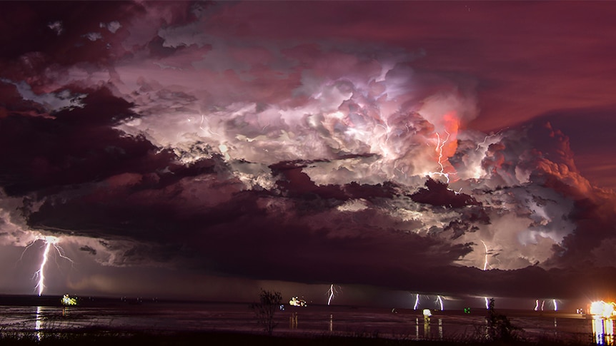 Night time photo of a lightning storm lighting up clouds over Broome, with multiple lightning strikes hitting the ground.