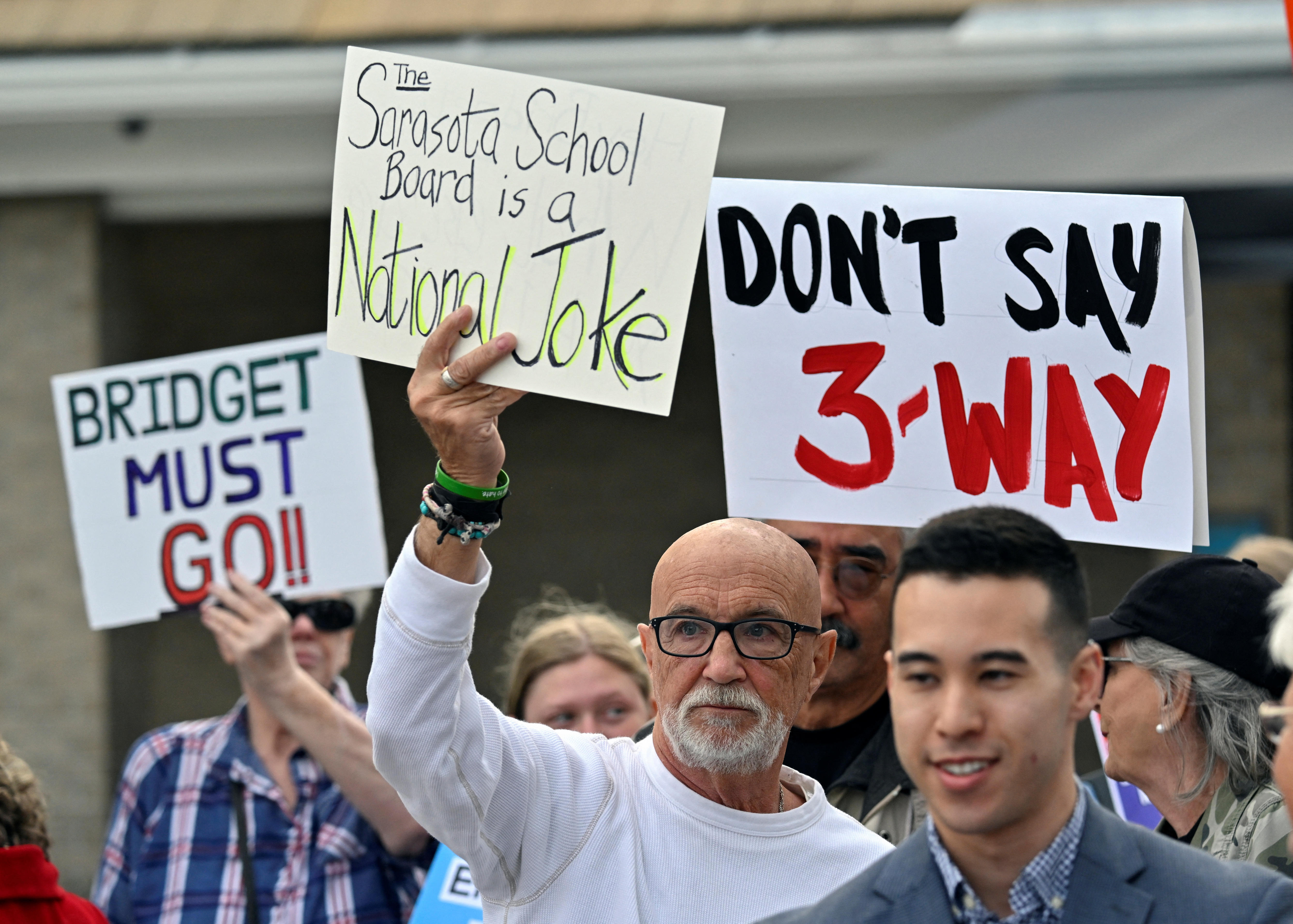 People hold protest signs with messages like 'Bridget must go' and 'Don't say 3-way'.