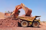A digger is filling up a truck with iron ore in the NT.