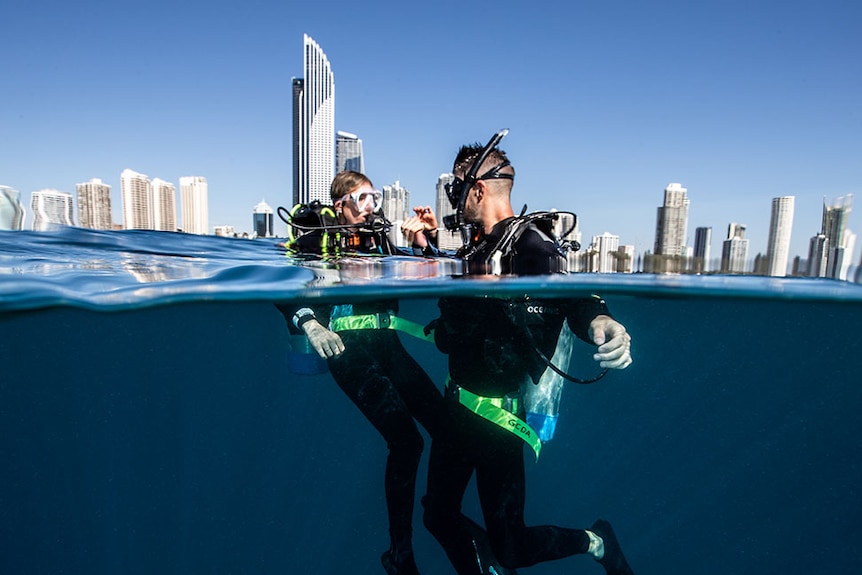 Man and woman scuba divers on surface of water with city skyline in background.