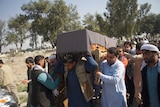 A group of men carry a wooden coffin covered in black fabric above their heads.