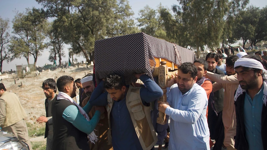 A group of men carry a wooden coffin covered in black fabric above their heads.