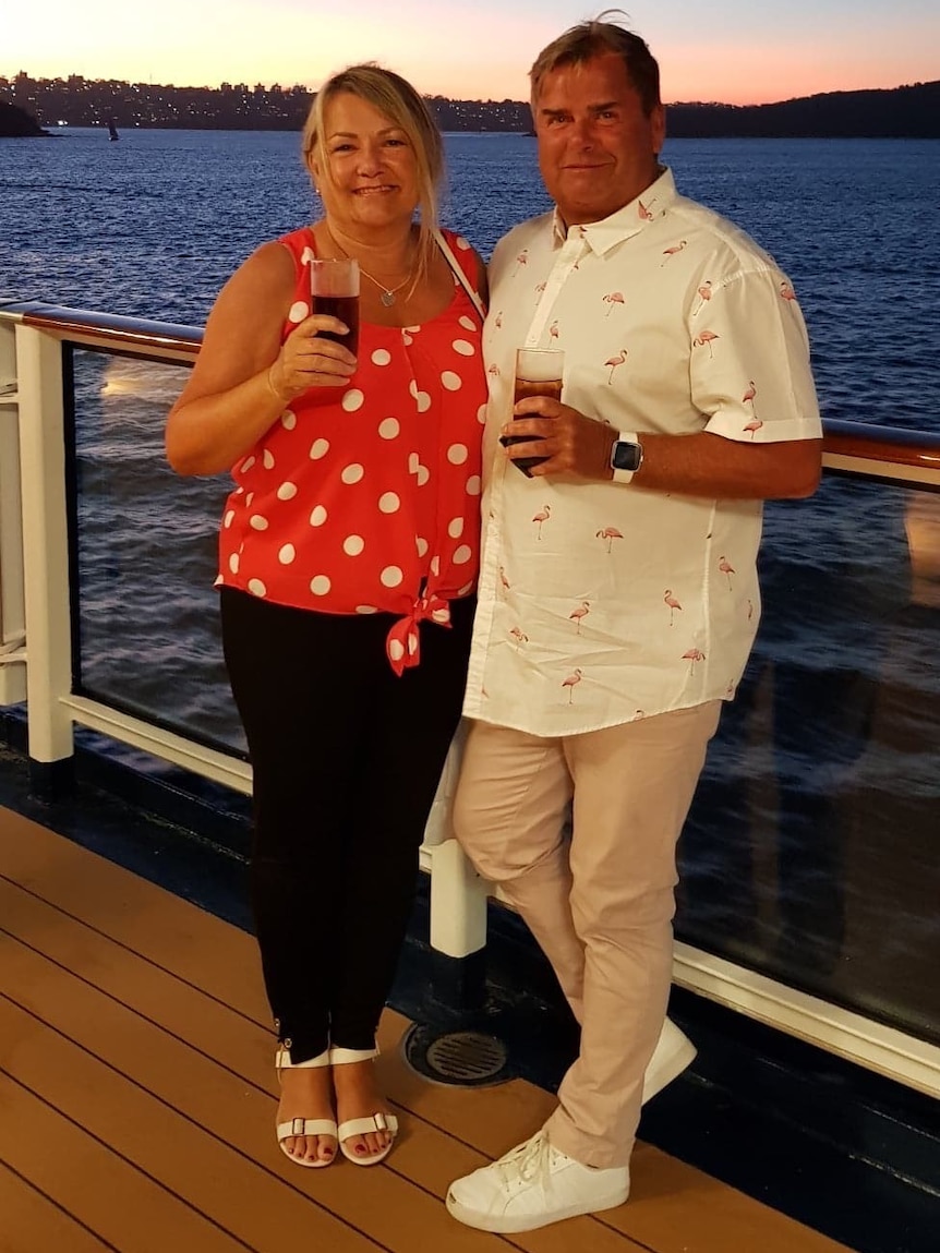 A woman and a man holding glasses on a deck in front of water