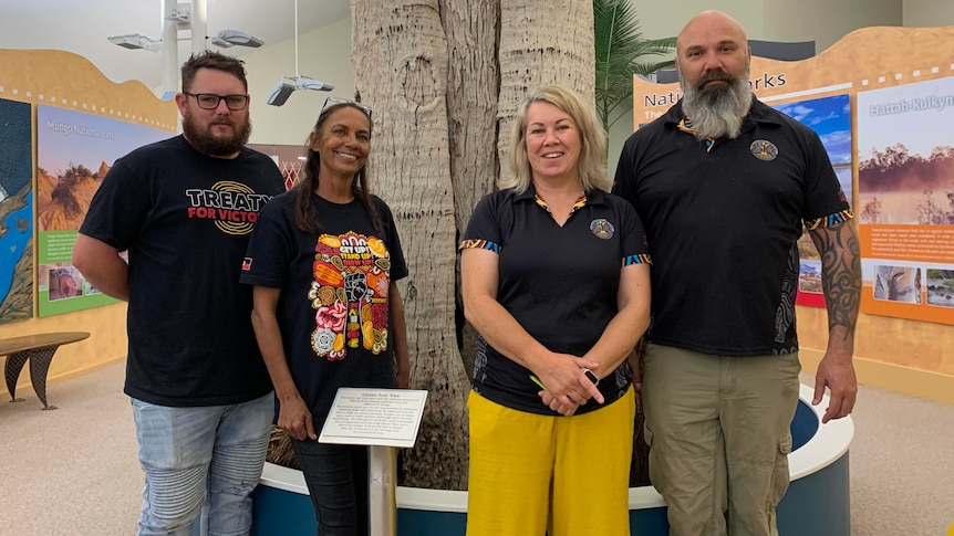 Four people stand in front of an Indigenous scar tree