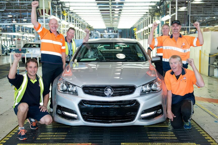 Holden workers smile as they surround a Commodore in the factory.