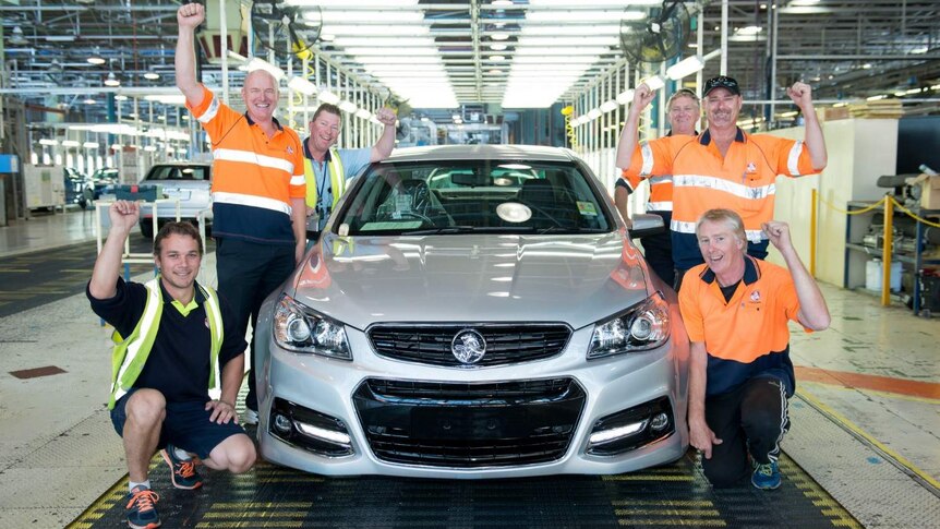 Holden workers smile as they surround a Commodore in the factory.