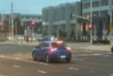 Blue car sits at traffic lights with apartment buildings by the side of road.